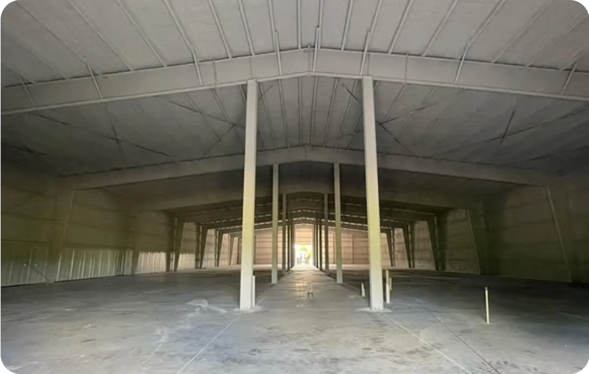 A finished commercial shell with spray foam covering the full roof deck and every wall, concrete columns down the centre and a bare slab floor